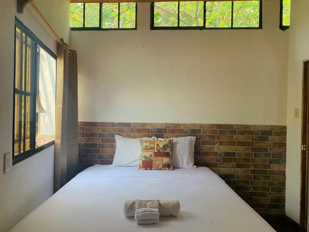 a bedroom with a white bed with two windows at Hostal Raíces de mi Pueblo in Suchitoto