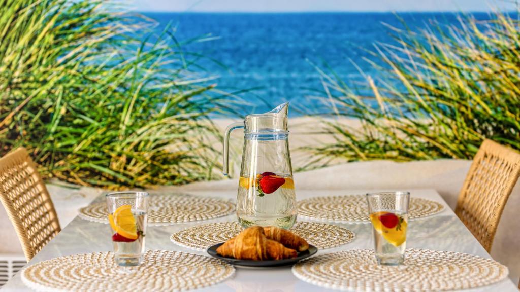 Dining table with pitcher, glasses and croissant, beach mural backdrop suggesting seaside breakfast