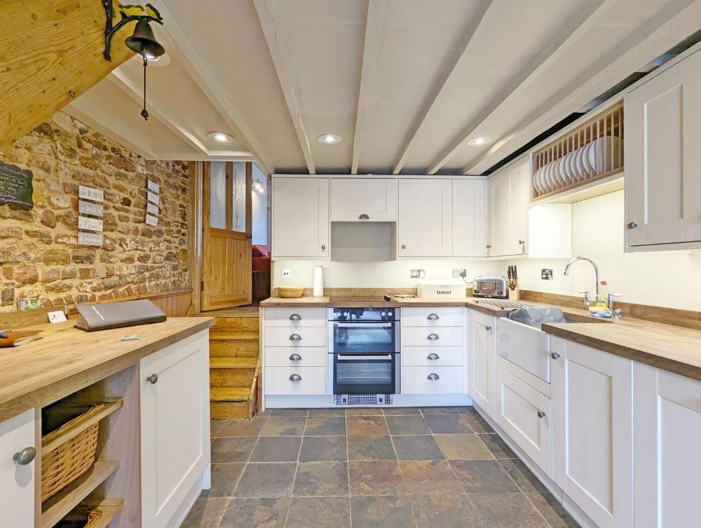 a kitchen with white cabinets and a stone wall at Piemans Cottage in Pulborough