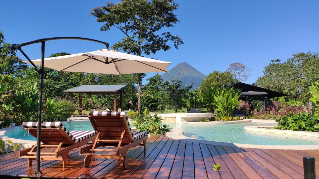 a deck with two chairs and an umbrella next to a pool at Hotel Arenal Glamping in Fortuna
