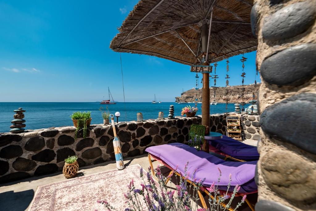 a patio with chairs and an umbrella and the ocean at Serenity Blue (Cave house) in Akrotiri