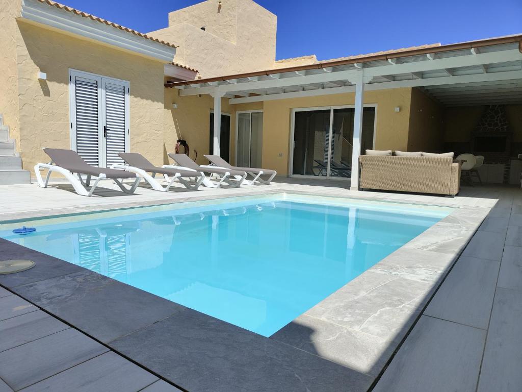 uma piscina com cadeiras e uma casa em villa bonita em Corralejo