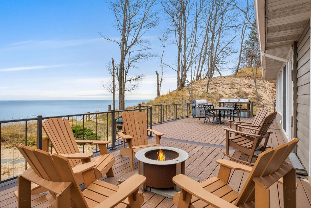 a deck with rocking chairs and a fire pit at Lakefront House with Private Beach by Michigan Waterfront Luxury Properties in Norton Shores