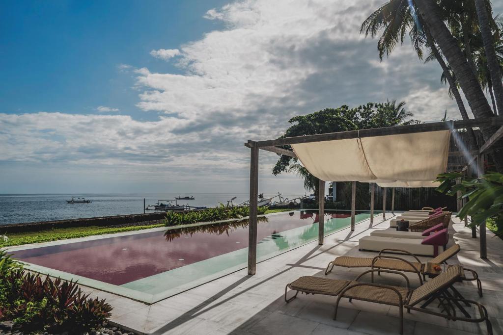 a swimming pool with chairs and the ocean in the background at The Tiing Tejakula Villas in Tejakula