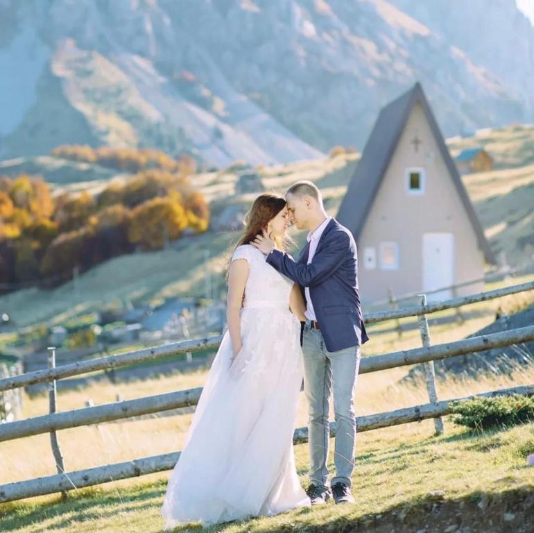 Una novia y un novio besándose en una colina con un granero en Vikendica Komovi, en Andrijevica