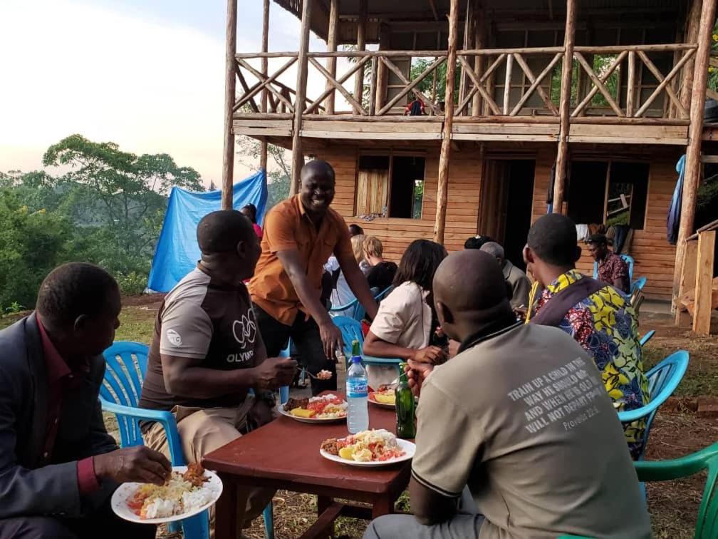 a group of people sitting around a table eating food at Noah's Ark Campsite & Restaurant in Fort Portal