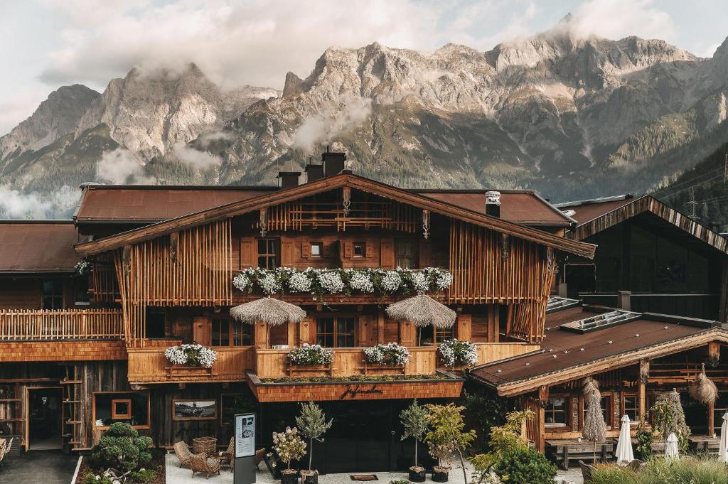 a large wooden building with flowers on it in front of mountains at Jufenalm BOHO Hotel & Restaurant in Maria Alm am Steinernen Meer