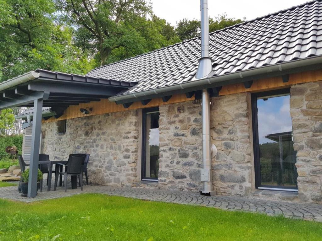 a stone house with a black roof and a patio at NEU! Modernes Ferienhaus Hohensayn in Lautzenbrücken
