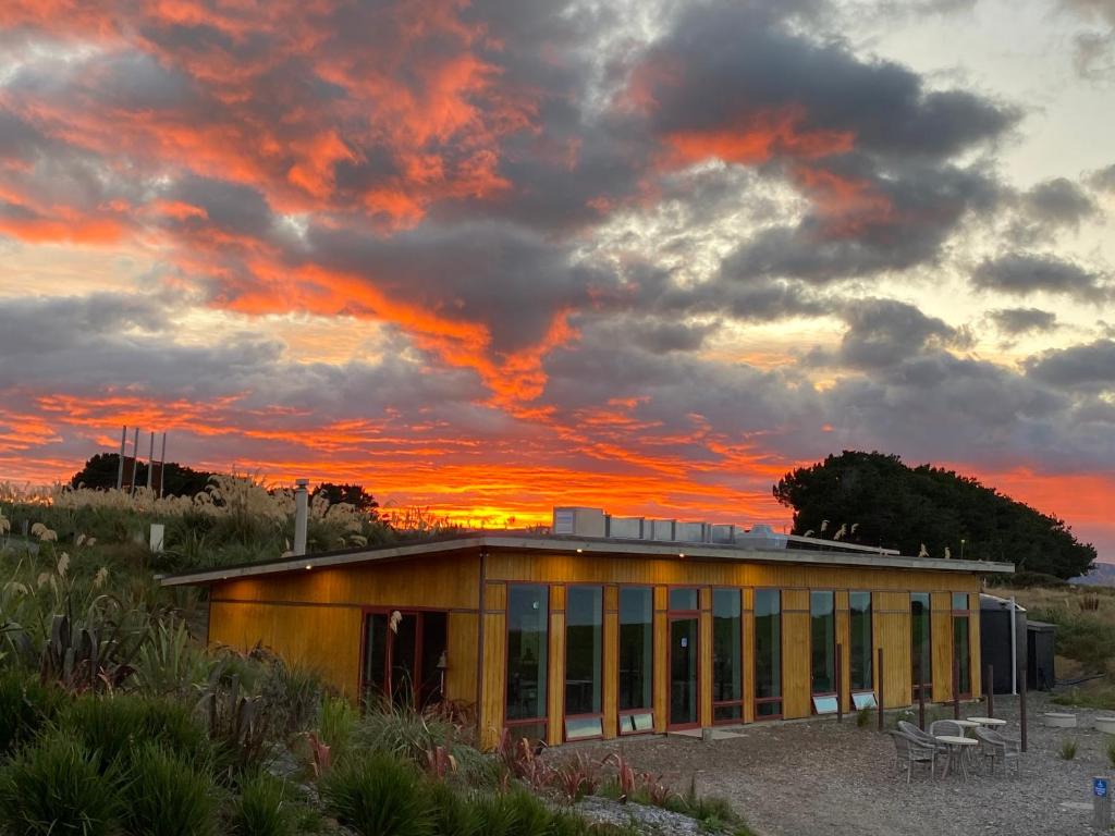 a building on the beach with a sunset in the background at The Cliffs Seaside Lodge in Tuatapere