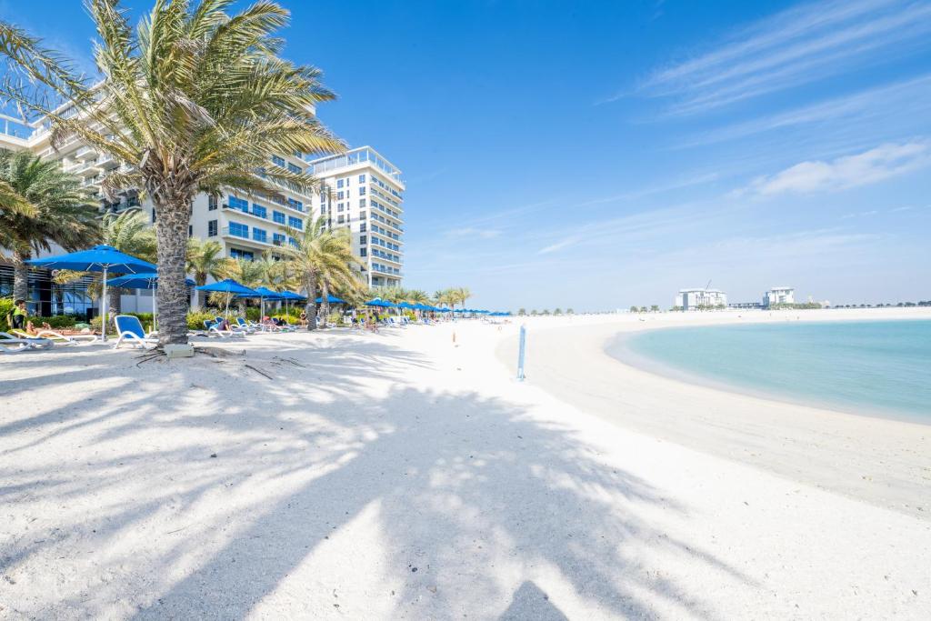 a white beach with palm trees and the ocean at Luxury 1BR Beachfront Apartment Marjan Island in Ras al Khaimah