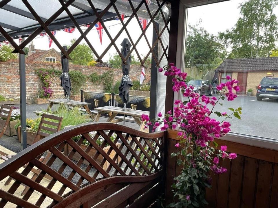 un banco de madera en un porche con flores rosas en The Star Inn, en Nafferton