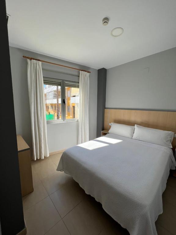 a bedroom with a large white bed and a window at Hostal Manuela in Punta Umbría