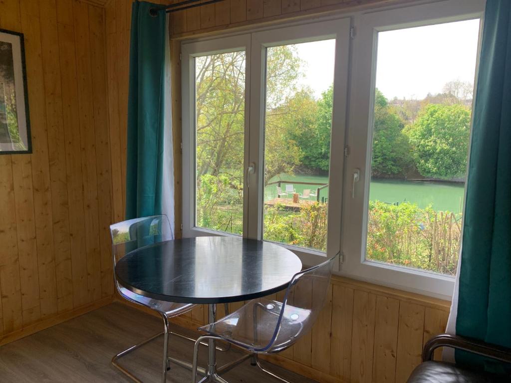 een tafel en stoelen in een kamer met 2 ramen bij chalet paradisiaque en bord de Marne Proche de Disneyland in Isles-lès-Villenoy
