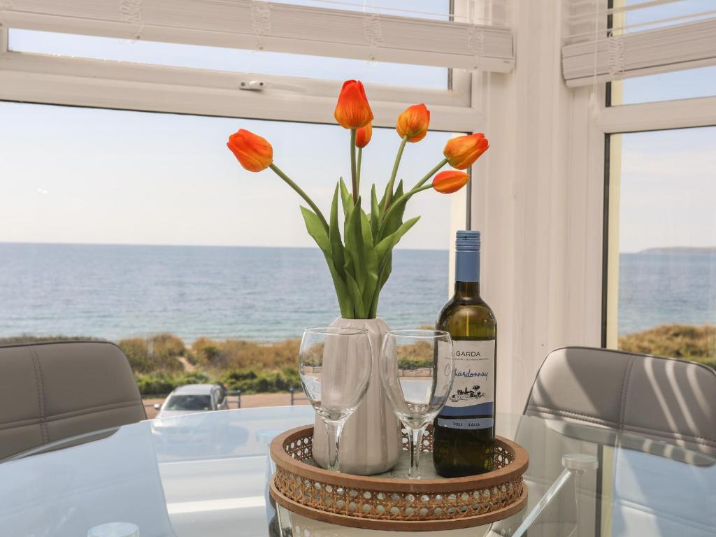 a table with a vase of flowers and a bottle and glasses at Tir a Mor in Pwllheli