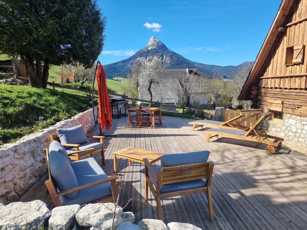 un patio con sillas y mesas con una montaña en el fondo en gîte Le Maz'eau avec jacuzzi, en Saint-Pierre-de-Chartreuse