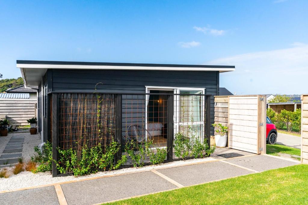 een zwart gebouw met een hek in een tuin bij Marram Studio - Mangawhai Holiday Studio in Mangawhai