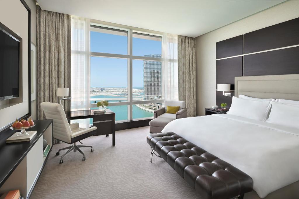 a hotel room with a bed and a desk and a large window at Rosewood Abu Dhabi in Abu Dhabi