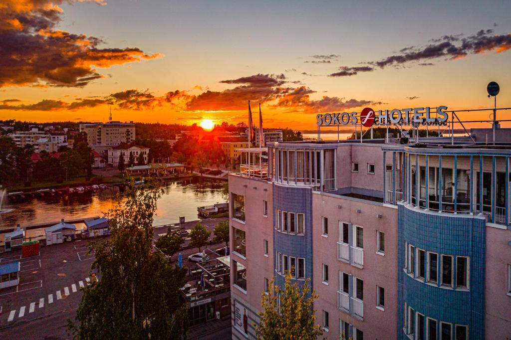 Original Sokos Hotel Seurahuone Savonlinna في سافونلينّا: غروب الشمس على مدينة بها مبنى ونهر
