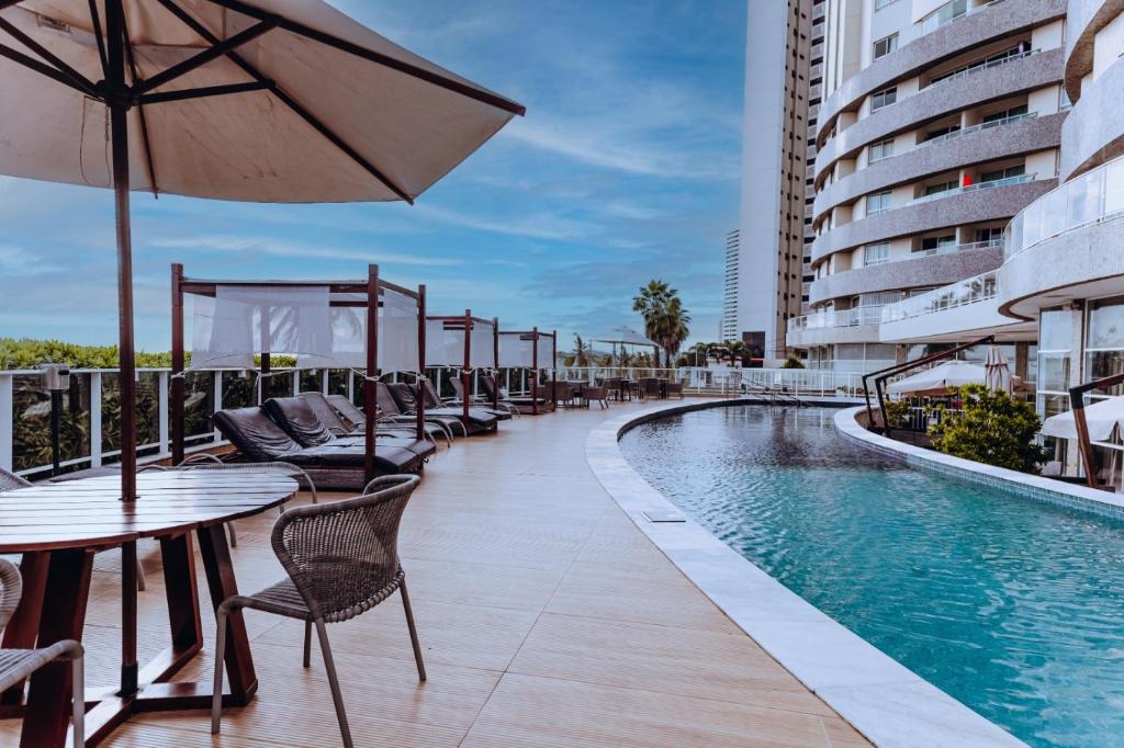 uma piscina com mesas e cadeiras ao lado de um edifício em Golden Tulip Natal Ponta Negra em Natal