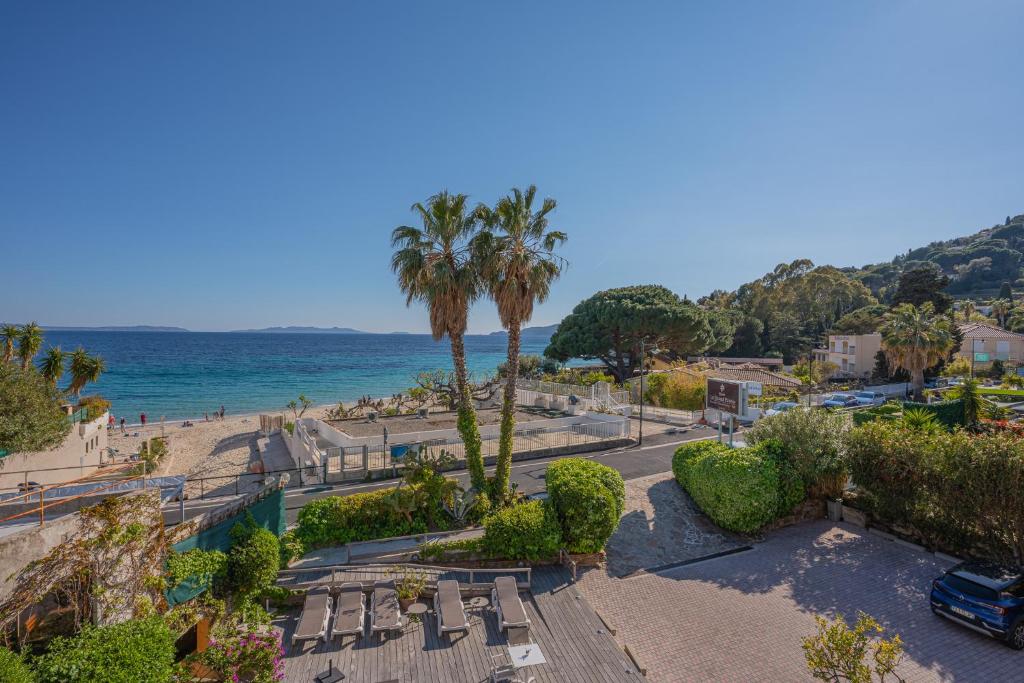 uma praia com cadeiras e palmeiras e o oceano em Hotel Le Grand Pavois em Le Lavandou