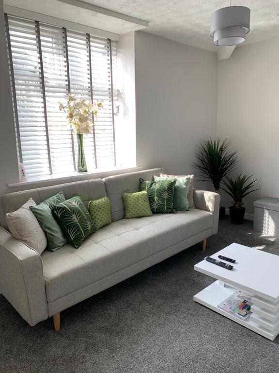 uma sala de estar com um sofá cinzento com almofadas verdes em The Greens Apartment em Farnworth