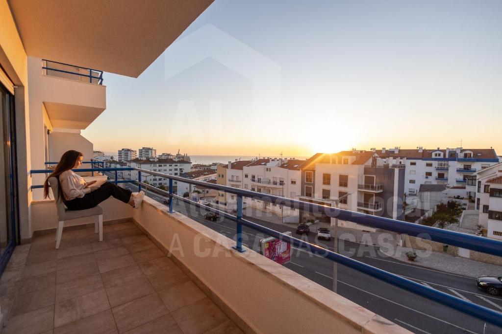 a woman sitting on a chair on a balcony watching the sunset at Home Sweet Home by ACasaDasCasas in Ericeira