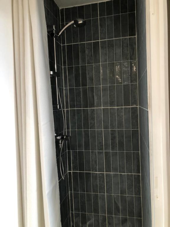 a shower with black tiled walls and a shower curtain at Chez julie in Caen