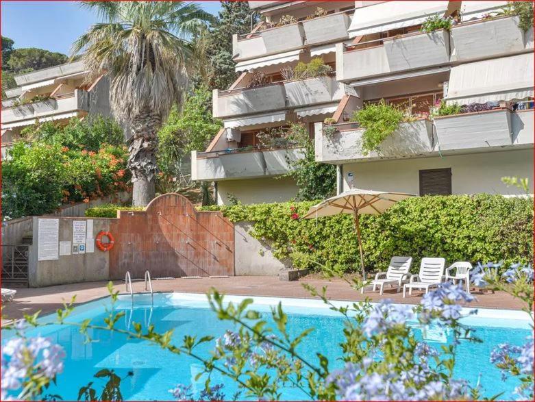 una piscina con sillas y una sombrilla frente a un edificio en Appartamenti La Colombaia, en Porto Azzurro
