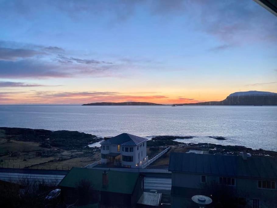 a view of the ocean and a house with the sunset at Newly renovated house with garden and ocean view in Tórshavn