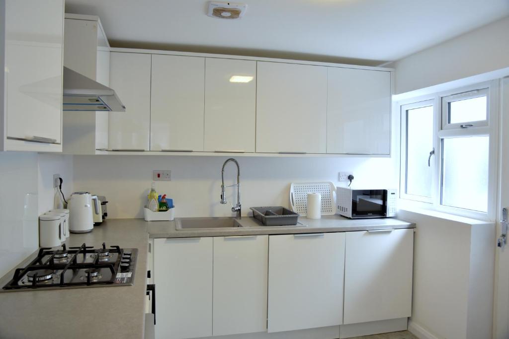 uma cozinha branca com armários brancos e um lavatório em Lindrick Villa- 3BD Bunglow , Free parking- Long stays em Leicester