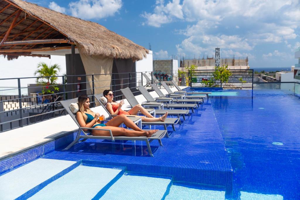 duas mulheres sentadas em espreguiçadeiras ao lado de uma piscina em Hotel 52 Playa del Carmen em Playa del Carmen