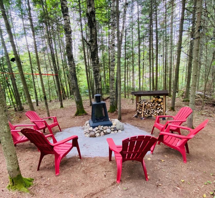 a group of red chairs and a fire pit in the woods at COZY CHALET WELL LOCATED in Saint-Faustin