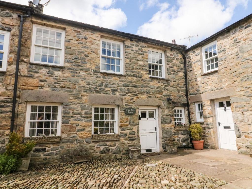 an old stone house with white doors and windows at Piggy Bank Cottage in Sedbergh