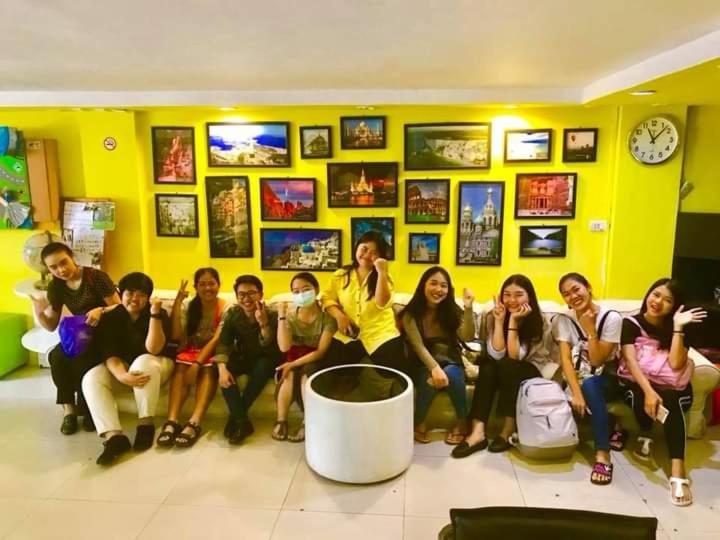 grupa ludzi siedzących przed żółtą ścianą w obiekcie VR hostel สะพานควาย w mieście Bang Su