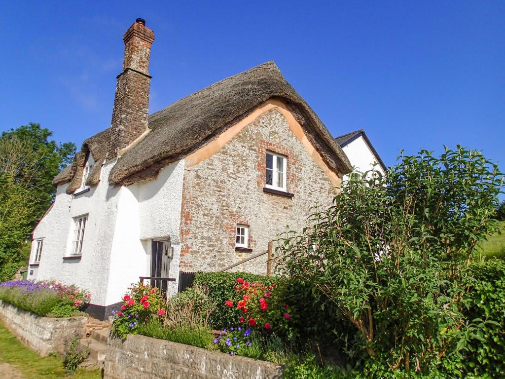 un cottage au toit de chaume avec des fleurs en face de lui dans l'établissement West Henstill House, à Crediton