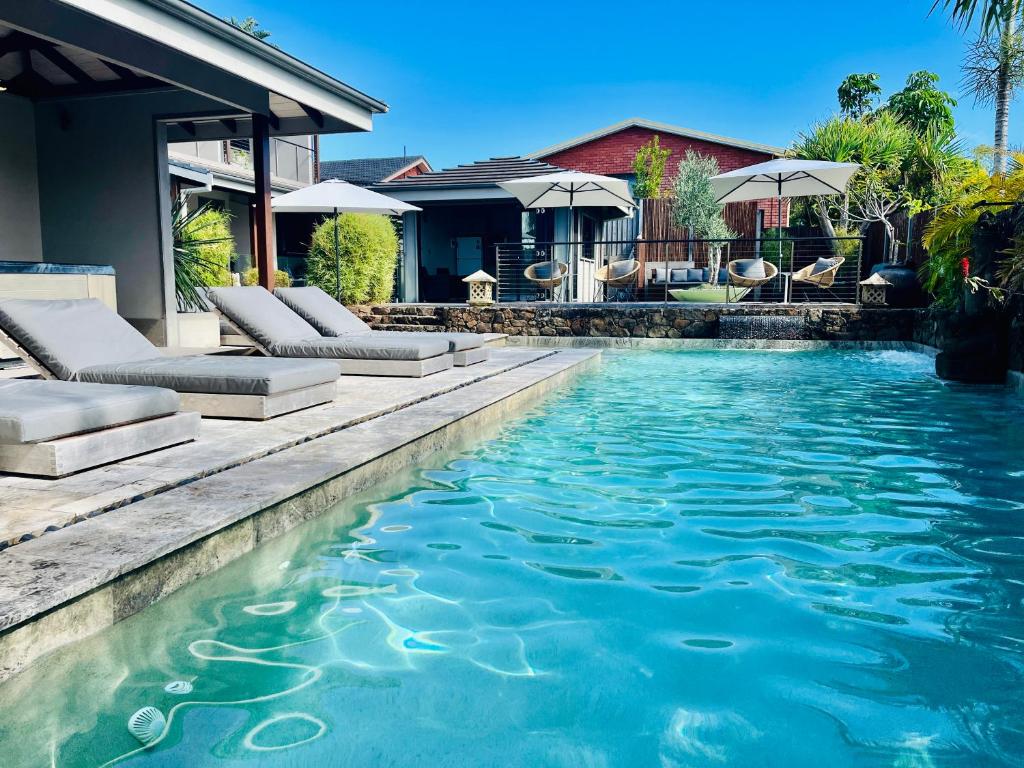a swimming pool with chairs and a house at Aabi's at Byron in Byron Bay