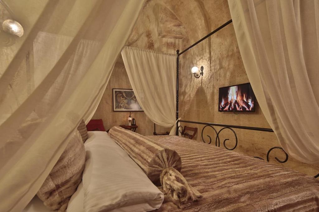 a bedroom with a canopy bed with a tv on the wall at Asuwari Suites Cappadocia in Ürgüp