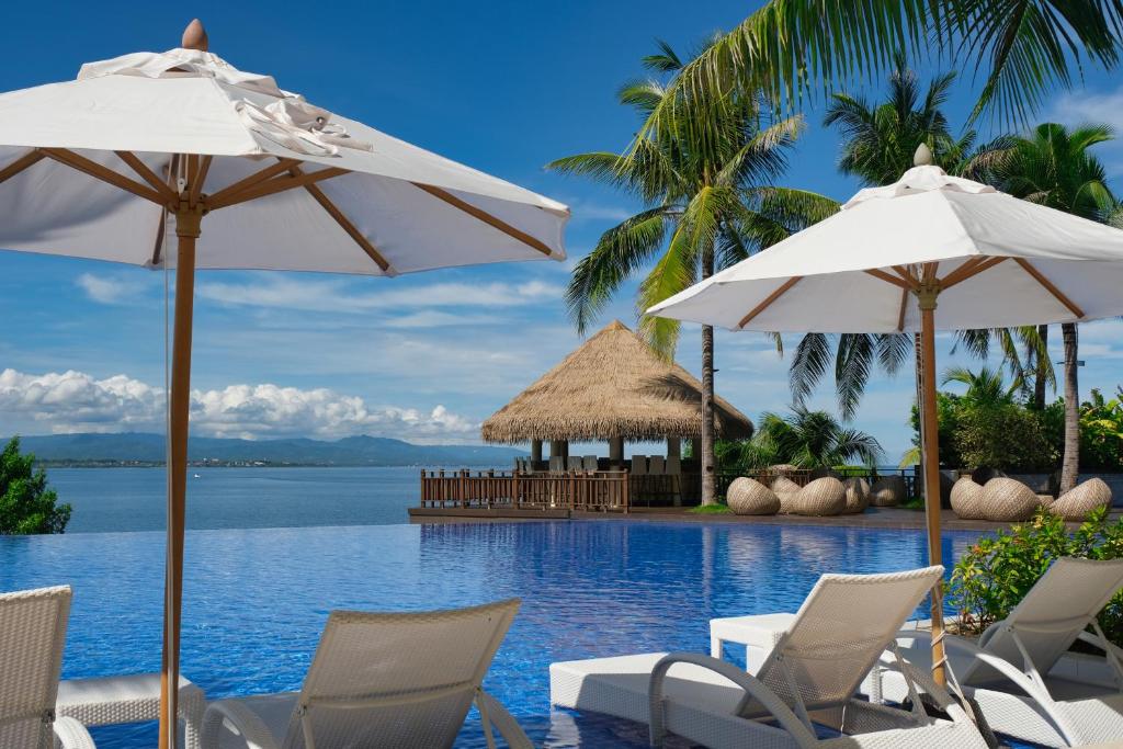 a resort swimming pool with chairs and umbrellas at Dusit Thani Mactan Cebu Resort in Mactan