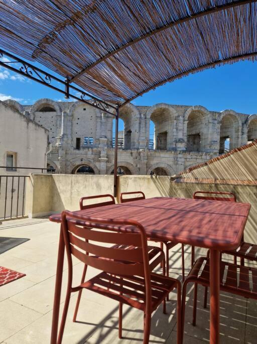 une table et des chaises en bois sous un toit dans l'établissement Les Arènes, à Arles