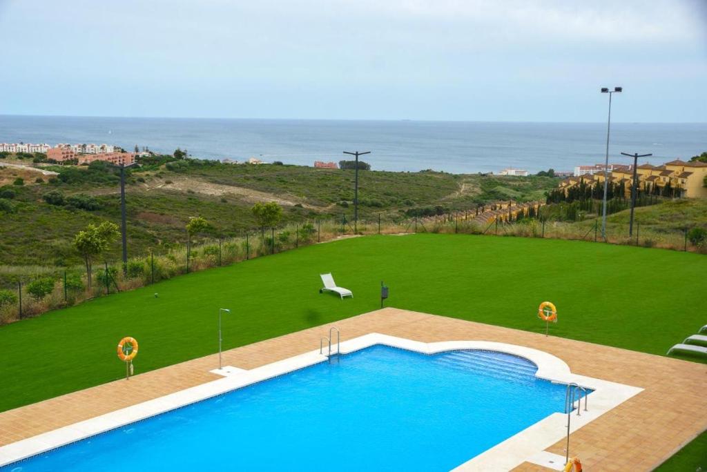a large swimming pool with a green field and the ocean at Small Oasis Nelson Mandela Apartment with sea view, two bedrooms, parking, terrace and pool in Manilva