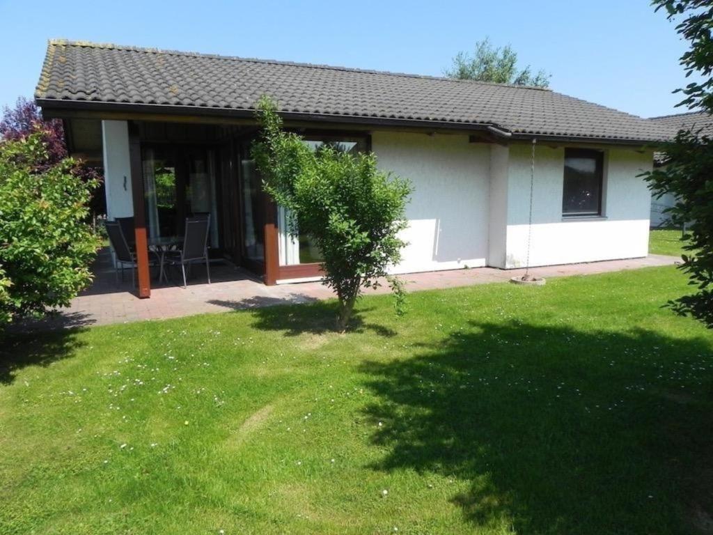 a house with a green lawn in front of it at J10 freistehendes Ferienhaus in Eckwarderhörne mit Terrasse eingefriedet durch Buchenhecke und Zaun in Butjadingen