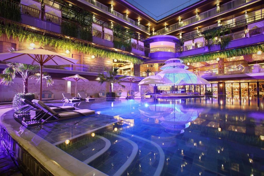 una piscina de hotel con sillas y sombrillas por la noche en The Crystal Luxury Bay Resort Nusa Dua, en Nusa Dua
