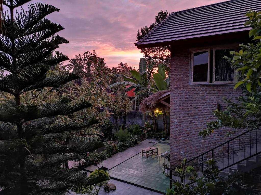 a house with a palm tree in front of a sunset at Les Rizieres Lombok - Tetebatu in Tetebatu