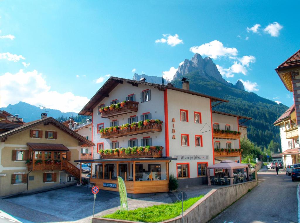 a large building in a town with mountains in the background at Hotel Aida in Pozza di Fassa