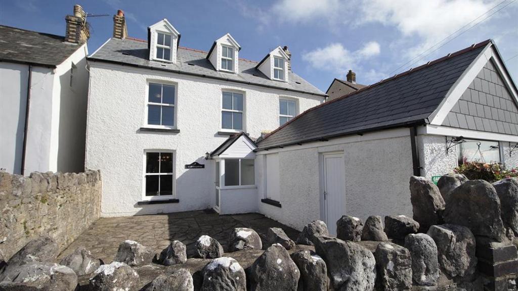 una casa blanca con una valla de piedra delante de ella en Carreg Lwyd Farmhouse, en Port Eynon
