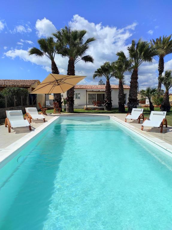 una piscina con sillas, sombrilla y palmeras en Villa Noemi, en Cava dʼAliga