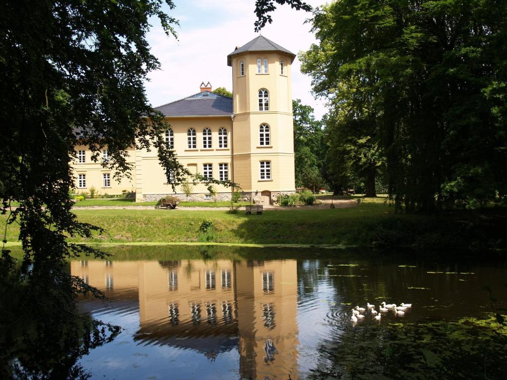 a large yellow building with a reflection in a pond at Landhaus Schloss Kölzow in Kölzow