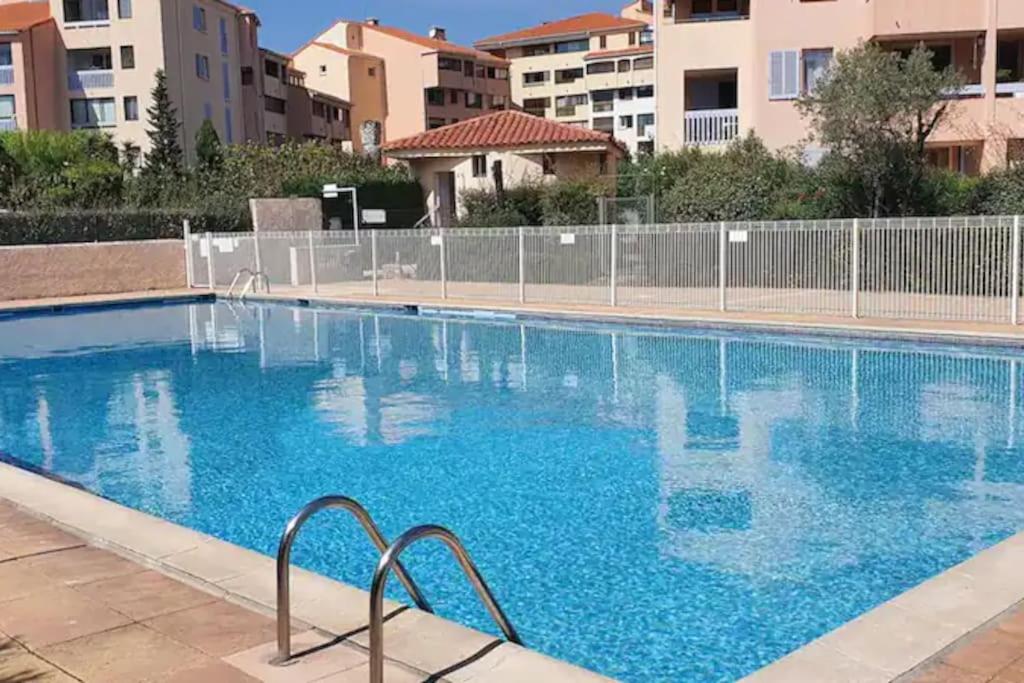 a large blue swimming pool with buildings in the background at Appartement spacieux 65M2, avec piscine et parking in Fréjus