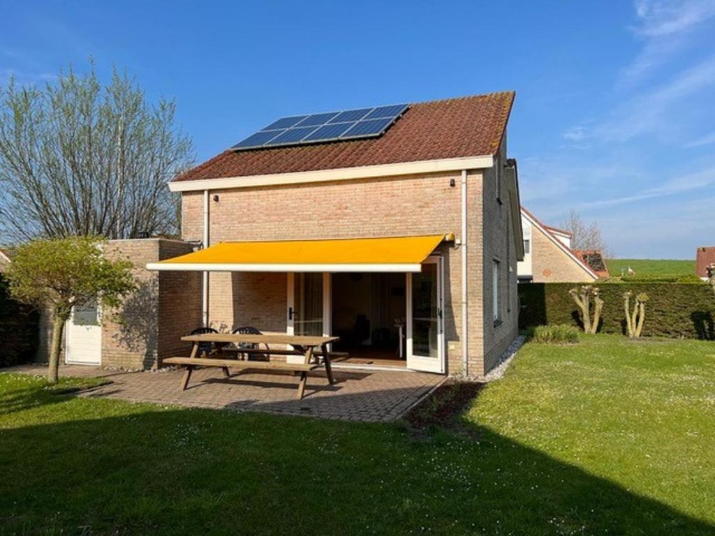 ein Haus mit einem Picknicktisch und einem Sonnendach in der Unterkunft Kustverhuur, Park Scheldeveste, Schelde 76 in Breskens