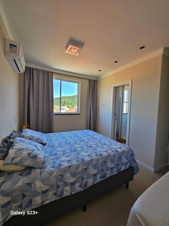 - une chambre avec un lit doté d'une couette bleue et d'une fenêtre dans l'établissement Cobertura em Bombinhas - Piscina - Luxo - Alto Padrão, à Bombinhas
